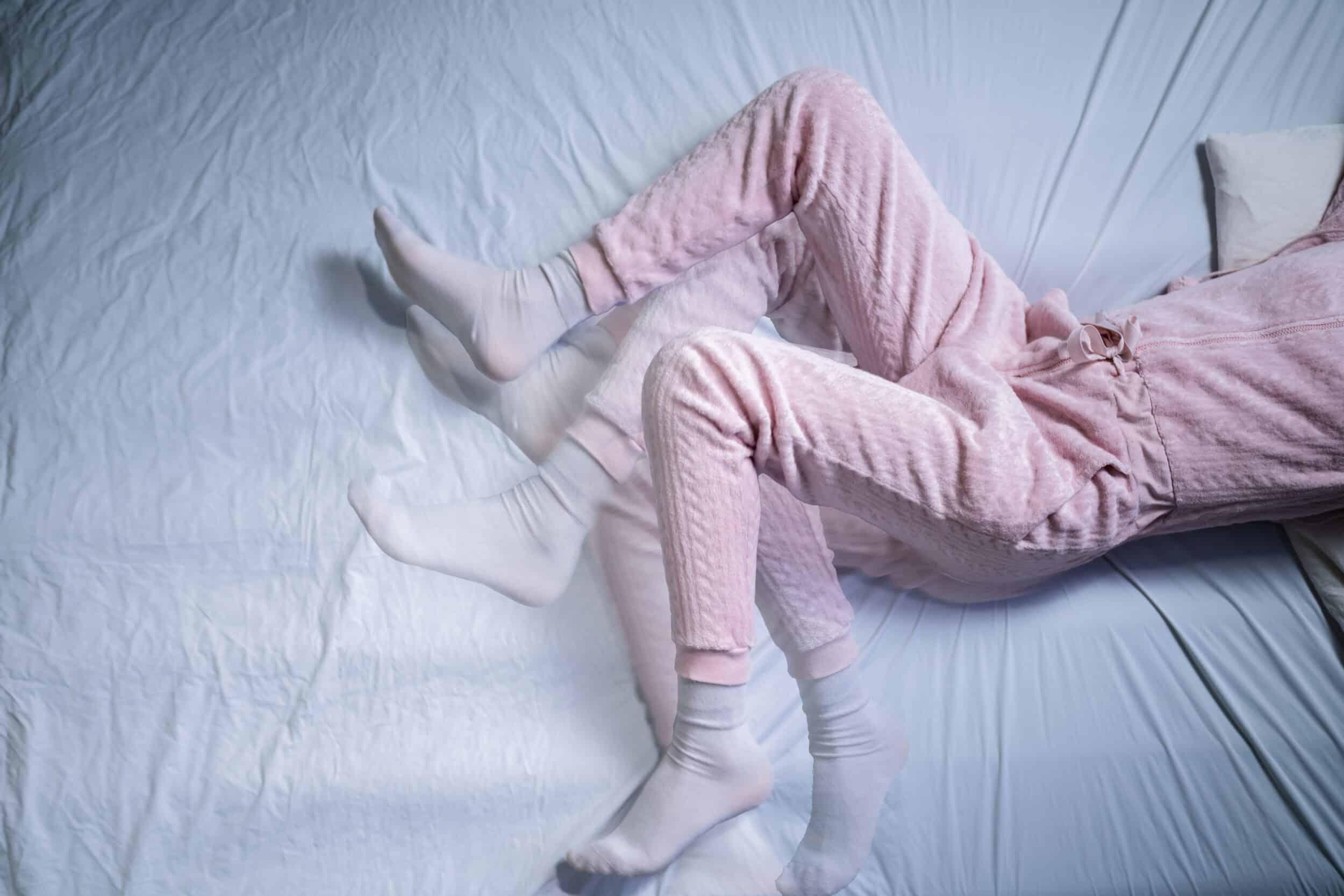 Woman in pink pajamas kicks her legs at night due to restless leg syndrome